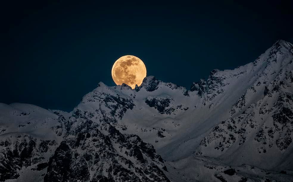 Pleine lune se levant derrière des sommets enneigés