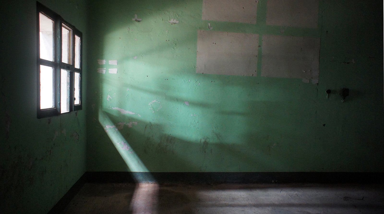 Pièce vide aux murs verts, un rai de lumière entrant par la fenêtre