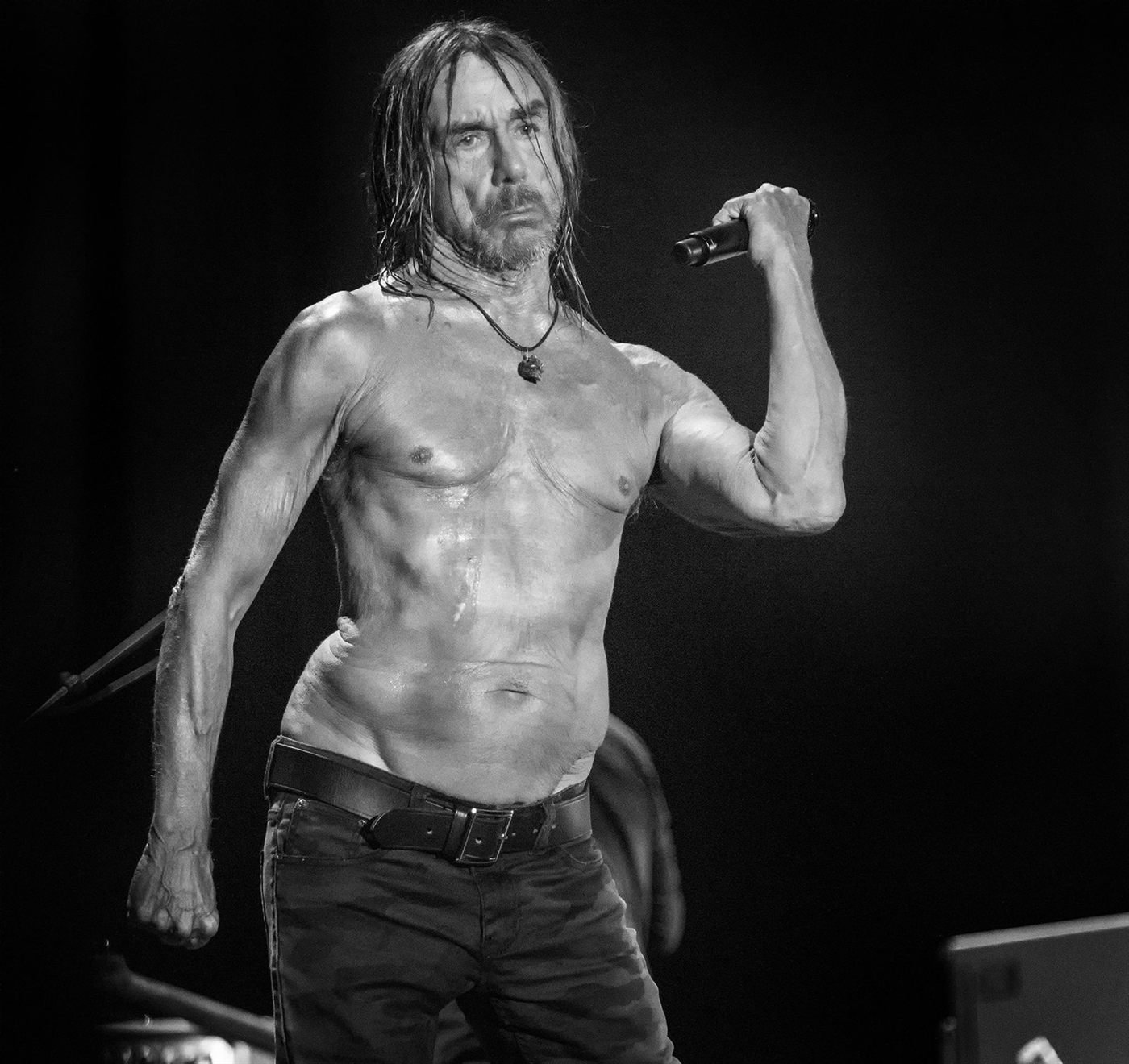 Chanteur torse nu sur scène, micro en main, en noir et blanc