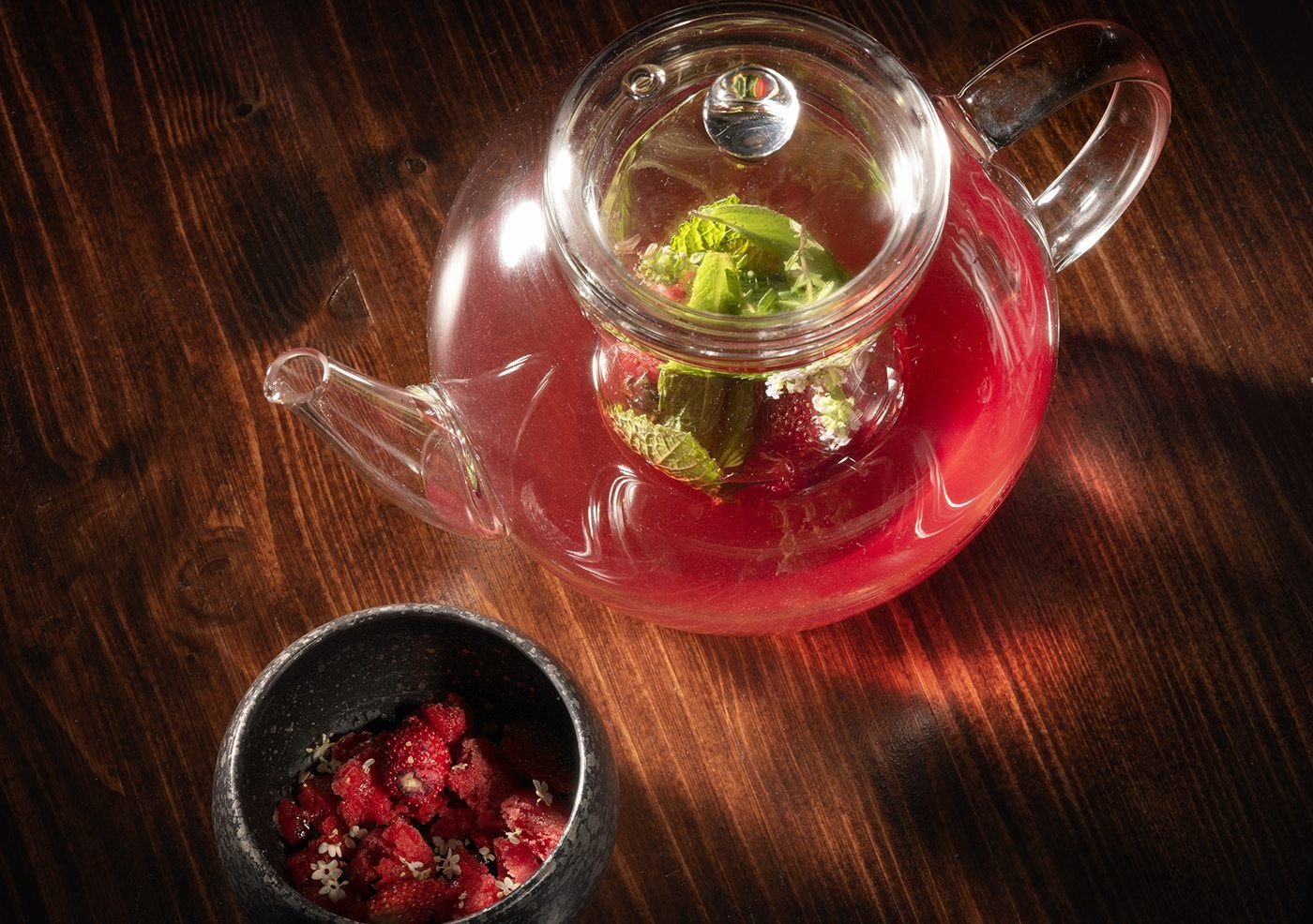 Théière en verre d'infusion aux fraises sur une table en bois sombre