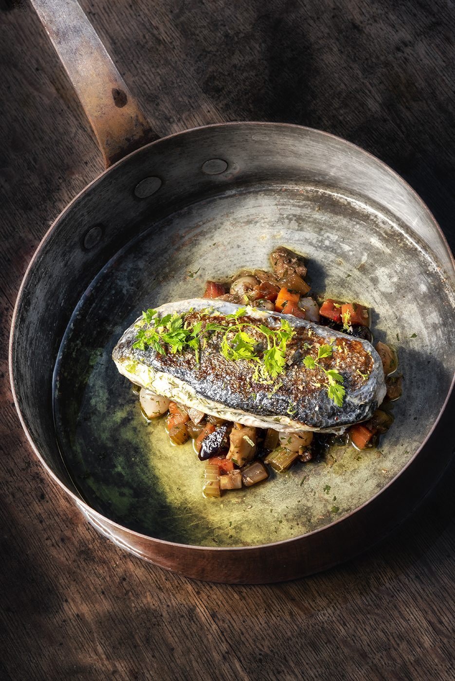 Filet de loup et petits légumes dans une poêle en cuivre