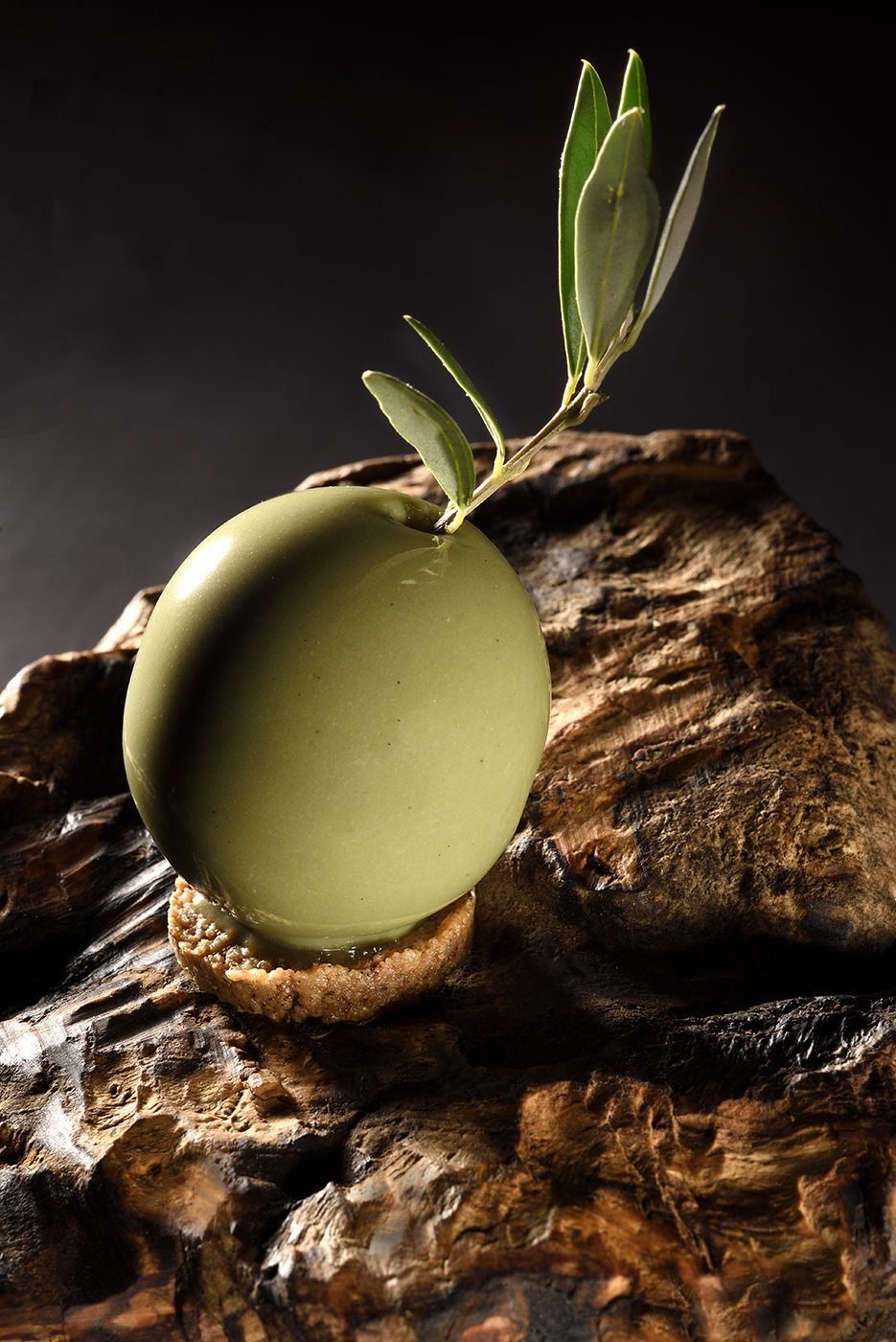 Dessert en trompe-l'œil en forme d'olive verte, posé sur une écorce
