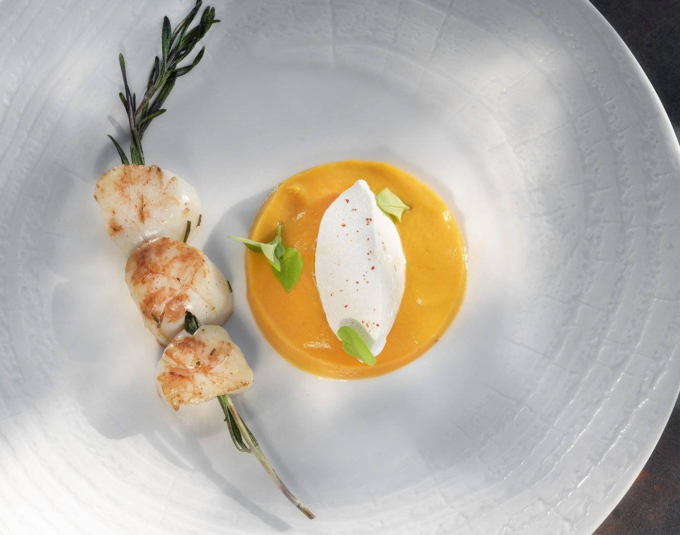 Brochette de noix de Saint-Jacques et sauce safranée dans une assiette blanche