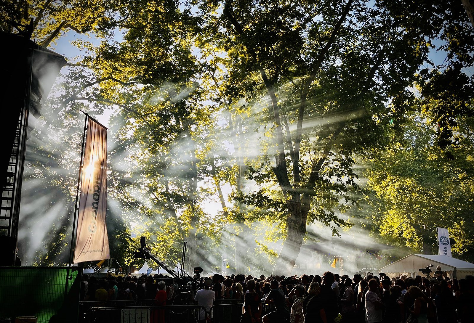 Public d'un festival à Grenoble sous les arbres, dans les rayons de lumière
