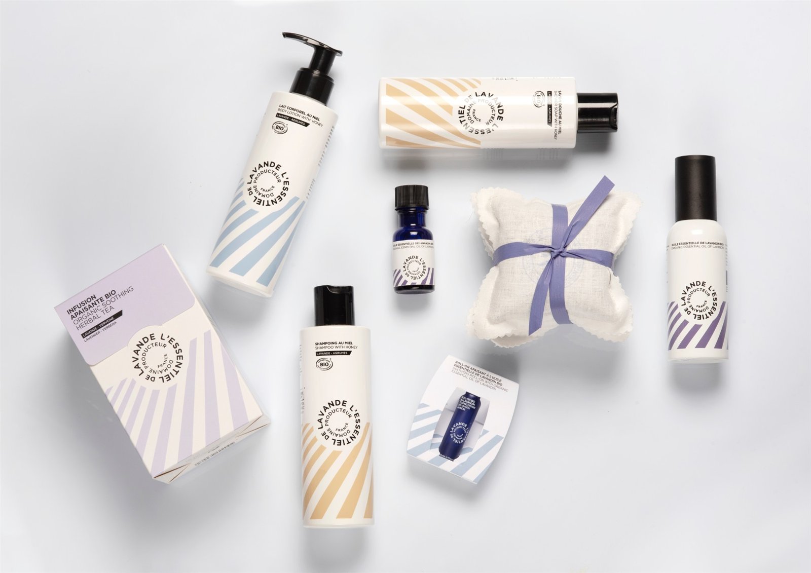 Gamme de soins bio à la lavande sur fond blanc : flacons, huile essentielle, roll-on, infusion et sachet noué d'un ruban violet